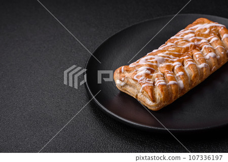 Delicious crispy braided bun with raisins inside and white icing outside 107336197