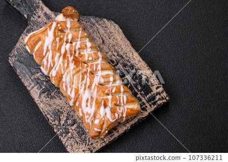 Delicious crispy braided bun with raisins inside and white icing outside 107336211