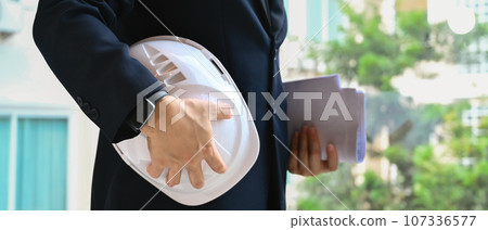 Architect man holding helmet and blueprints standing at a construction site Architect man holding helmet and blueprints standing at a construction site 107336577