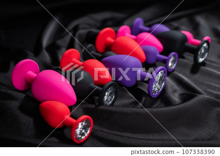 A set of silicone anal plugs in different colors and sizes on a black silk sheet. A set of silicone anal plugs in different colors and sizes on a black silk sheet. 107338390