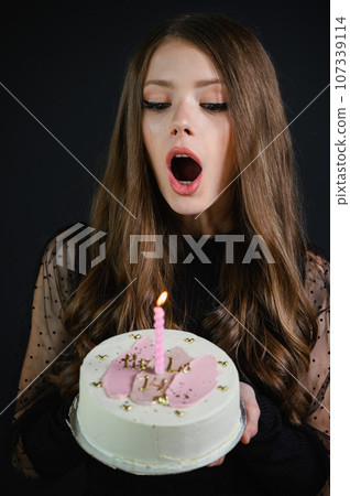 Happy teen girl wearing black dress blowing out a candle on a cake. Happy teen girl wearing black dress blowing out a candle on a cake. 107339114