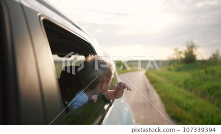 free boy kid hand from the window rides in a car wind in the face. conceptual journey of a car on the road. The boy son stretches out his hand from the car window, the sun glare of sunset lifestyle free boy kid hand from the window rides in a car wind in the face. conceptual journey of a car on the road. The boy son stretches out his hand from the car window, the sun glare of sunset lifestyle 107339394