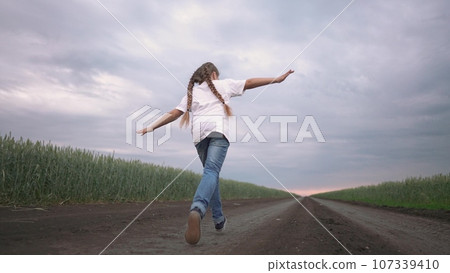 girl child running in nature in the park. happy family kid dream concept. free child daughter runs along a rural road next to a field in nature. free girl runs and plays in the park lifestyle girl child running in nature in the park. happy family kid dream concept. free child daughter runs along a rural road next to a field in nature. free girl runs and plays in the park lifestyle 107339410
