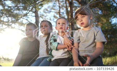 a group of children plays in a forest park. group of children close-up sitting on a log of a fallen tree. happy family child dream concept. A group of lifestyle children in a pioneer camp are playing 107339426