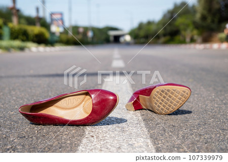Red women's shoes lying on the road in summer day 107339979