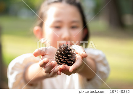 A child holding out a pine cone 107340285