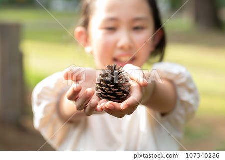 A child holding out a pine cone 107340286