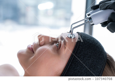 Young caucasian woman on microcurrent therapy procedure. Beautician's office. Young caucasian woman on microcurrent therapy procedure. Beautician's office. 107340708