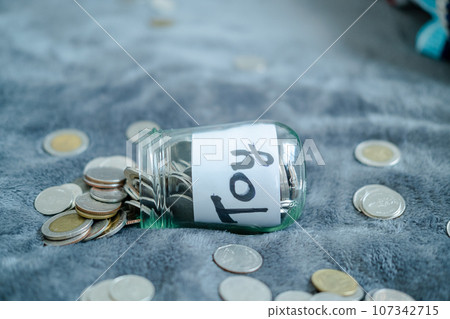 A glass bottle with the word toy on it. and silver coins for savings The glass is full until the glass falls. 107342715
