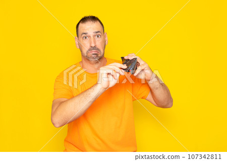 Financial crisis and bankruptcy due to the rise in prices of essential raw materials. Sad Spanish man showing empty wallet to camera, no money, spent money, yellow studio background. 107342811