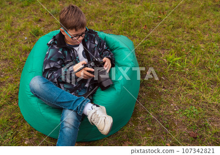 a boy with a camera is sitting on a green comfortable bag chair on the grass a boy with a camera is sitting on a green comfortable bag chair on the grass 107342821