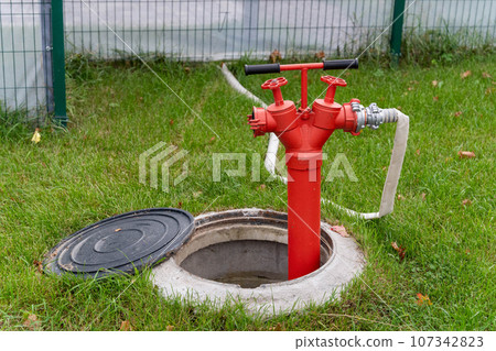 a street fire hydrant with a connected flexible fire hose. red iron fire hydrant a street fire hydrant with a connected flexible fire hose. red iron fire hydrant 107342823