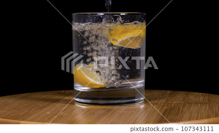 Close-up footage of soda and lemons pouring into glass on black background. Close-up footage of soda and lemons pouring into glass on black background. 107343111