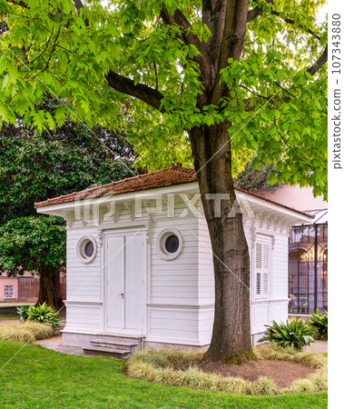 White wooden cottage with closed door and shuttered window pitched red bricks roof in a rural area White wooden cottage with closed door and shuttered window pitched red bricks roof in a rural area 107343880
