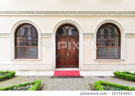 Wooden arched door between two arched windows in a stone beige wall Wooden arched door between two arched windows in a stone beige wall 107343881