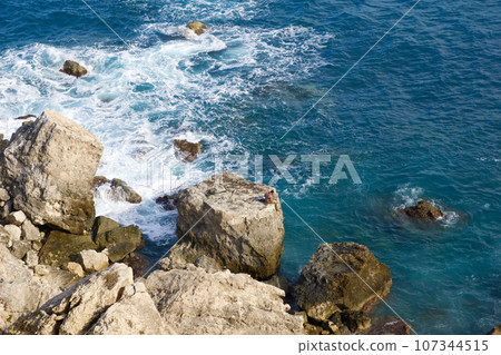 MELLIEHA, MALTA - 01 JAN, 2020: A man sitting on a rock near the ocean on the island of Malta during calm sea 107344515
