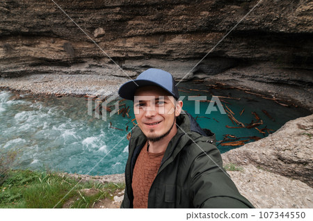 bearded Caucasian male traveler takes a selfie on smartphone against background of river in Aksu Canyon in Kazakhstan in spring 107344550