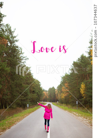 a girl in a pink raincoat and in rubber boots walks on the road in the middle of the forest-inscription love is 107344637