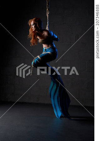 Young mermaid tied up in ropes against black background 107346888