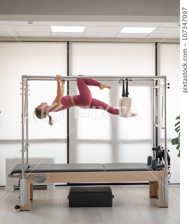 Beautiful asian woman in pink sportswear doing pilates on bed reformer.  107347097