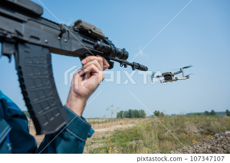 Man aiming to shoot a rifle at a flying drone outdoors. Man aiming to shoot a rifle at a flying drone outdoors. 107347107
