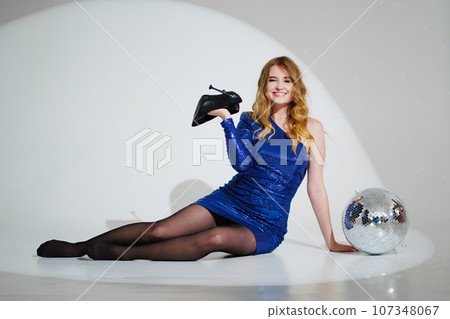 woman in shiny blue dress on floor with a disco ball on a white room 107348067