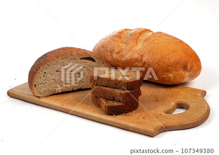 Bread lies on a wooden cutting board next to a knife on a white background. 107349380