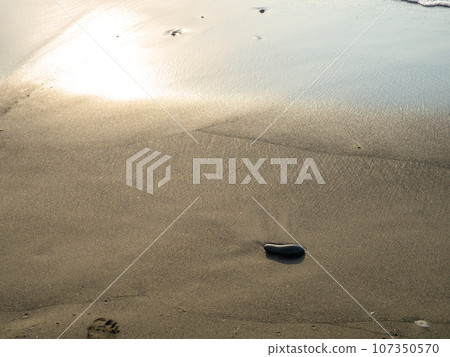 One stone on a background of black sand. The silence of the wild beach. Stones on the sandy beach. Black sand in the sun close-up. Quiet place. The silence of the waves Edge of the coast. Black sand 107350570