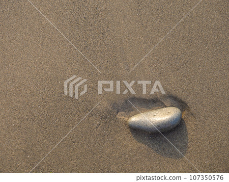 One stone on a background of black sand. The silence of the wild beach. Stones on the sandy beach. Black sand in the sun close-up. Quiet place. The silence of the waves Edge of the coast. Black sand 107350576