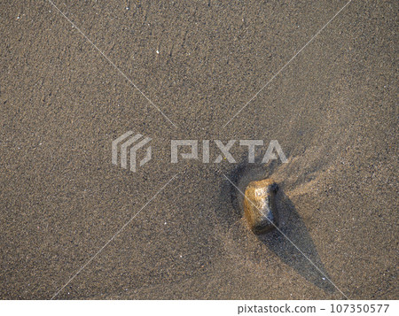 One stone on a background of black sand. The silence of the wild beach. Stones on the sandy beach. Black sand in the sun close-up. Quiet place. The silence of the waves Edge of the coast. Black sand 107350577
