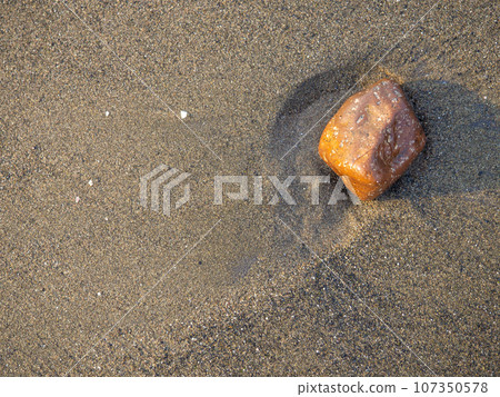 One stone on a background of black sand. The silence of the wild beach. Stones on the sandy beach. Black sand in the sun close-up. Quiet place. The silence of the waves Edge of the coast. Black sand 107350578