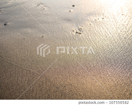 Wet sand of the beach in the rays of the setting sun. The silence of the wild beach. Natural background. Black sand in the sun close-up. Quiet place. Edge of the coast. Bathing place. Wet sand of the beach in the rays of the setting sun. The silence of the wild beach. Natural background. Black sand in the sun close-up. Quiet place. Edge of the coast. Bathing place. 107350582