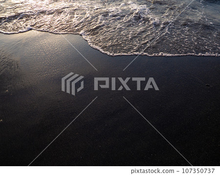 Wet sand of the beach in the rays of the setting sun. The silence of the wild beach. Natural background. Black sand in the sun close-up. Quiet place. Edge of the coast. Bathing place. Wet sand of the beach in the rays of the setting sun. The silence of the wild beach. Natural background. Black sand in the sun close-up. Quiet place. Edge of the coast. Bathing place. 107350737