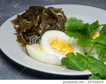 Seaweed salad and cut boiled egg. Dish on the table in a plate. Peppered half of an egg. parsley as decoration 107350879