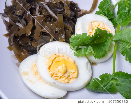 Seaweed salad and cut boiled egg. Dish on the table in a plate. Peppered half of an egg. Parsley greens as decoration. Seaweed salad and cut boiled egg. Dish on the table in a plate. Peppered half of an egg. Parsley greens as decoration. 107350880
