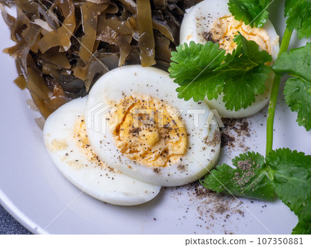 Seaweed salad and cut boiled egg. Dish on the table in a plate. Peppered half of an egg. Parsley greens as decoration. Seaweed salad and cut boiled egg. Dish on the table in a plate. Peppered half of an egg. Parsley greens as decoration. 107350881