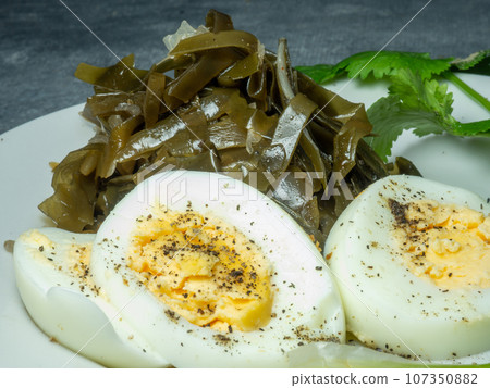 Seaweed salad and cut boiled egg. Dish on the table in a plate. Peppered half of an egg. Parsley greens as decoration. Seaweed salad and cut boiled egg. Dish on the table in a plate. Peppered half of an egg. Parsley greens as decoration. 107350882