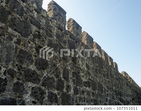 Remains of an old castle. Wall with teeth. Ancient fortifications made of stone. Museum in the open air. Wall of a medieval castle. Background from ancient stonework. 107351011