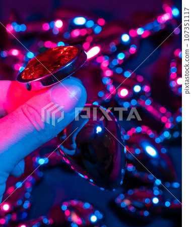 Man holding metal anal plug in neon pink purple light. Man holding metal anal plug in neon pink purple light. 107351117
