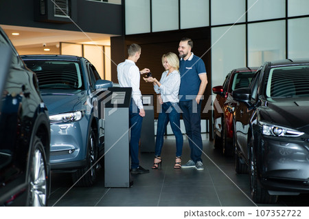 The seller hands over the car keys to the buyers. The couple bought a new car. The seller hands over the car keys to the buyers. The couple bought a new car. 107352722