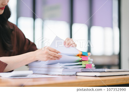 Businesswoman sifting through stacks of paper files and folders that contain both incomplete and completed documents. Selective focus 107352990