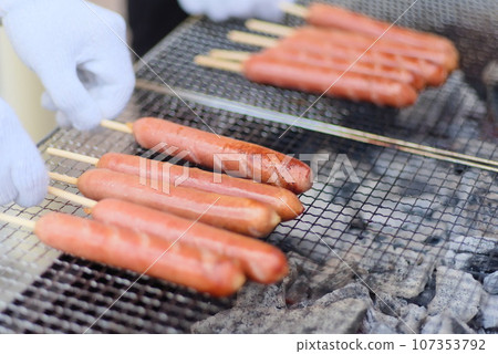 A lot of frankfurters being grilled over charcoal 107353792