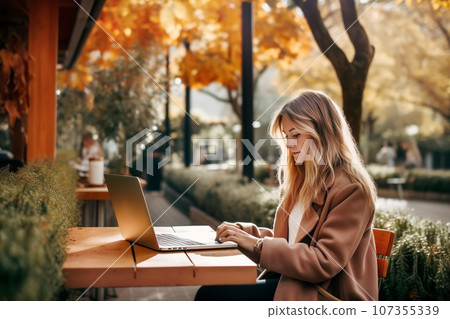 Attractive young woman working at a street cafe table on a warm autumn day Attractive young woman working at a street cafe table on a warm autumn day 107355339