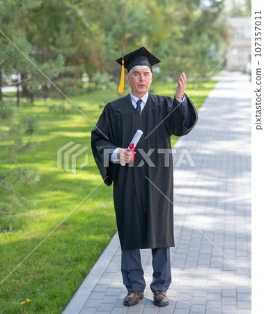 Serious old man in graduation gown holding diploma outdoors. Serious old man in graduation gown holding diploma outdoors. 107357011
