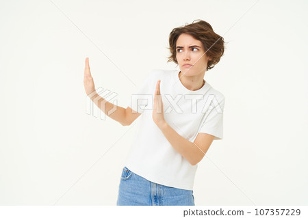 Portrait of woman avoiding someone, shows block hands gesture and refusing from something bad, standing over white background Portrait of woman avoiding someone, shows block hands gesture and refusing from something bad, standing over white background 107357229