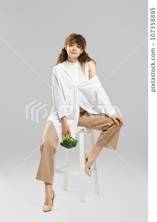 Beautiful woman with broccoli sits on chair 107358895