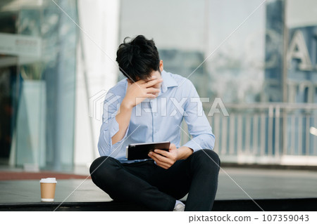 Frustrated young Asian businessman working on a laptop computer sitting at his working place in outside office 107359043