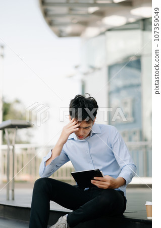 Frustrated young Asian businessman working on a laptop computer sitting at his working place in office Frustrated young Asian businessman working on a laptop computer sitting at his working place in office 107359049