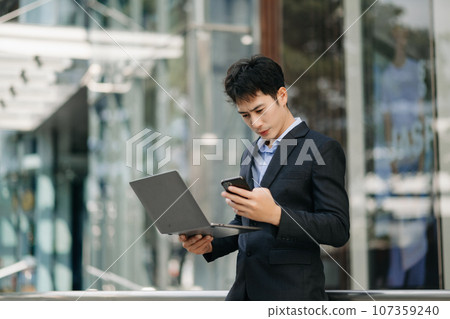 Confident Asian man with a smile standing holding notepad and tablet at the modern office.. Confident Asian man with a smile standing holding notepad and tablet at the modern office.. 107359240