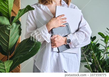 A woman holds a laptop and graphics tablet against a background of greenery. 107359775